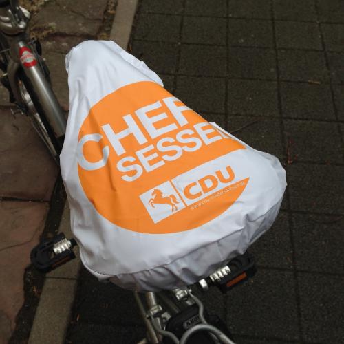 Sattelschutzhülle aus weißem PVC. Bedruckt mit weißer Schrift auf Orange: Chef Sessel.