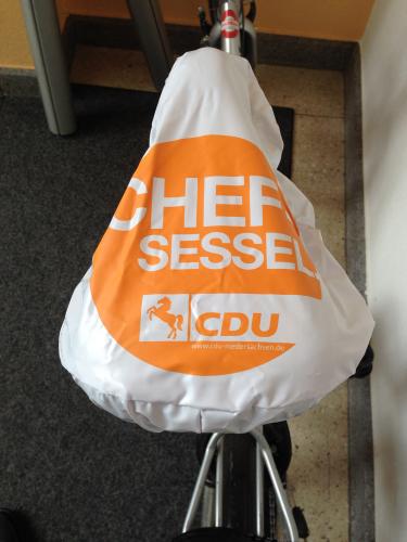 Sattelschutzhülle aus weißem PVC. Bedruckt mit weißer Schrift auf Orange: Chef Sessel.