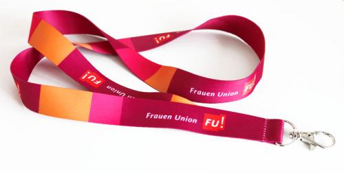 Liegendes Umhängeband bunt bedruckt in den Farben Rot, Magenta, Orange und Aubergine. Aufdruck: FU! Frauen Union. Band mit Karabinerverschluss.
