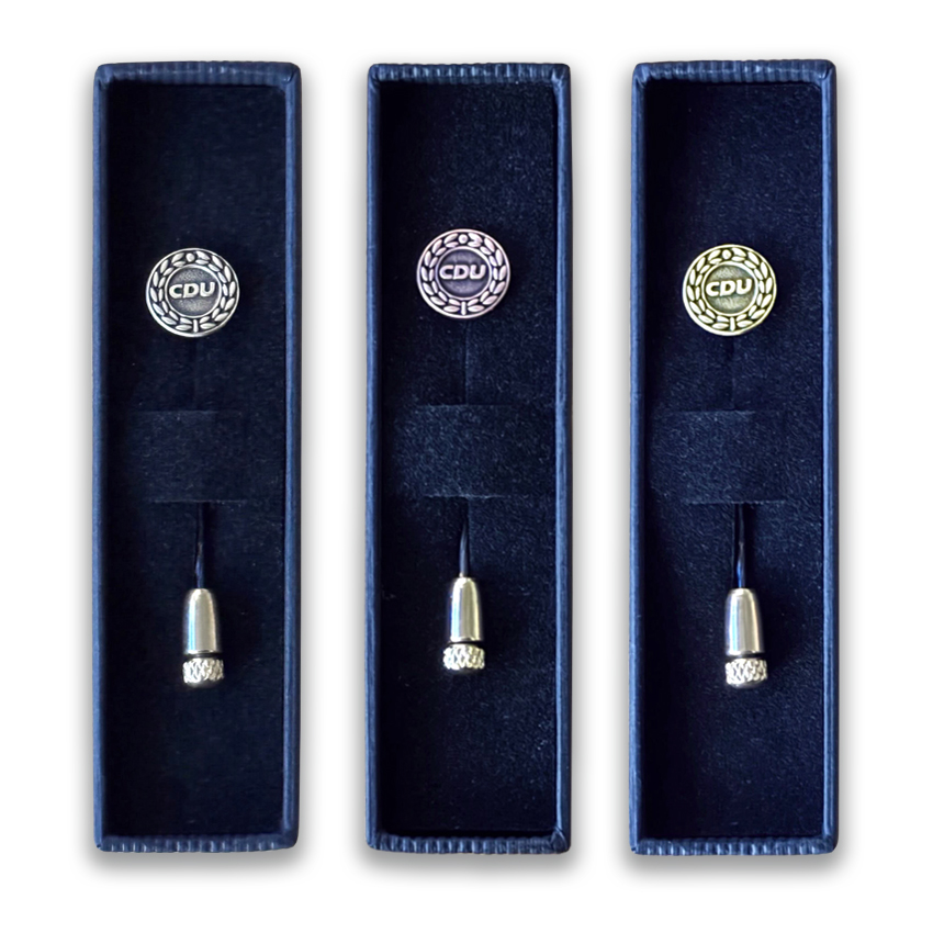 Drei offene Kartonschachteln in Schwarz. In jeder Schachtel ist eine Ehrennadel eingesteckt.